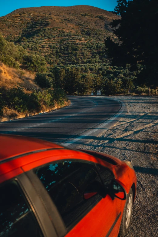 a red car driving past a forest on the side of the road