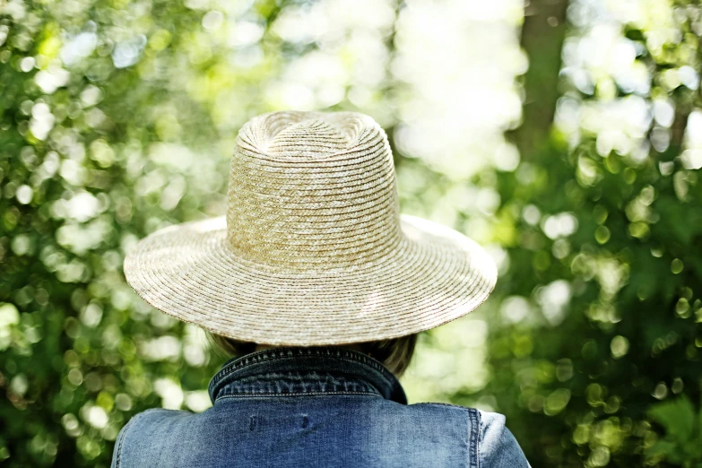 person with hat looking away in sunlight with trees in background