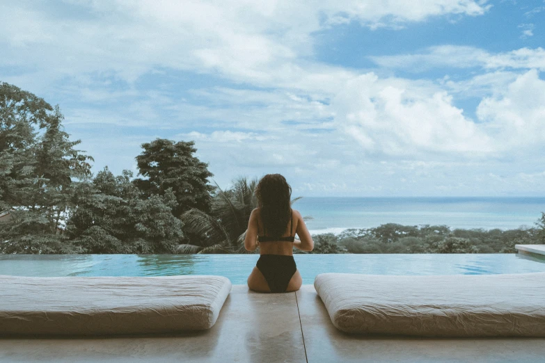 the girl is sitting by the pool watching the water