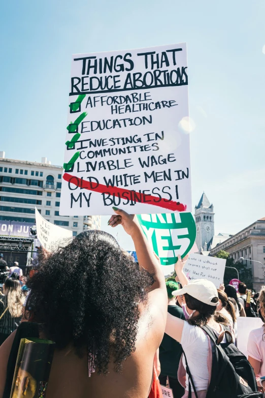 a woman holds a sign as people hold a rally