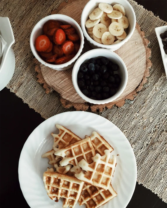 bananas, blueberries, strawberries and coffee sit next to two plates of waffles