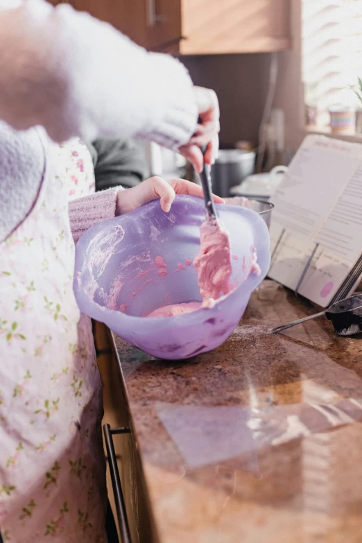 a person in an apron uses a spoon to dip food into the pink bowl