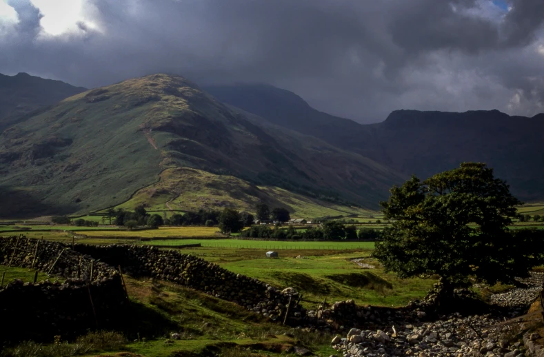 a field and mountains with dark clouds above