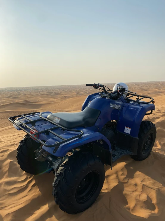 a blue four - wheeler with four tires is in the sand