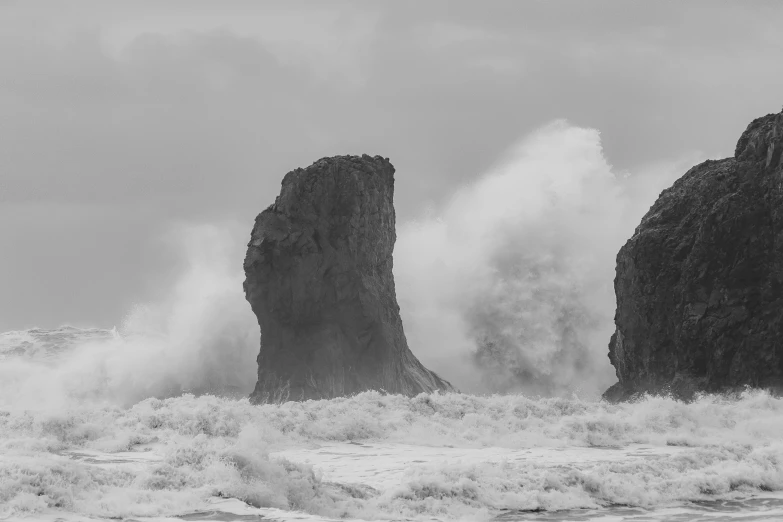 black and white pograph of an ocean crashing against large rock formations