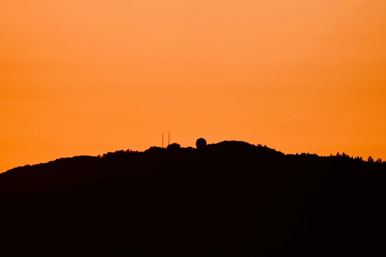 a mountain is silhouetted at sunset with an orange sky