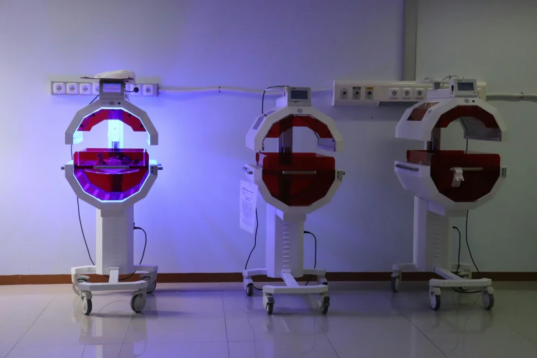 three red, white and blue shaped medical machines standing on casters in a room