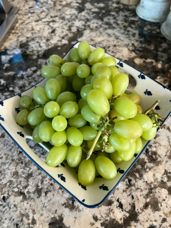 a bunch of green gs is in a blue and white square bowl on the table