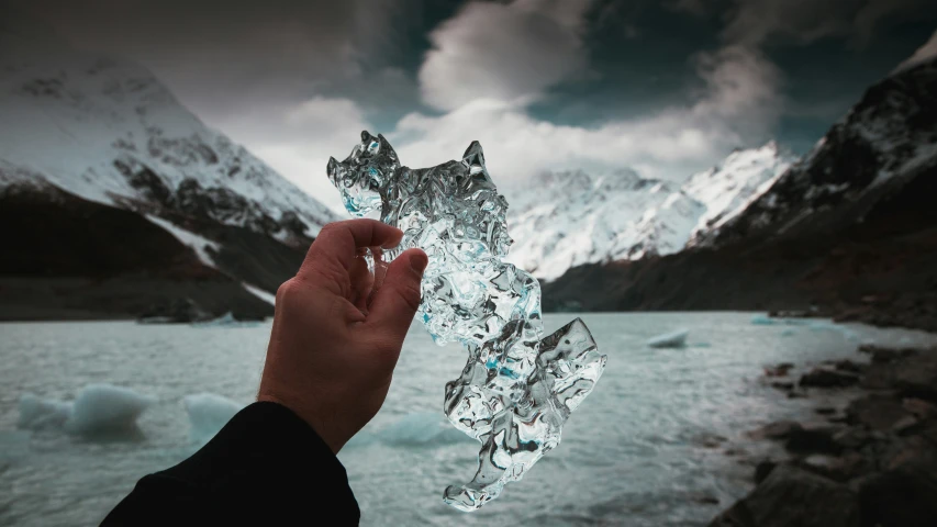 the hand holding up the ice block in front of a mountain lake