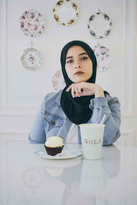 a woman in hijab sitting at a table with a cup and plate