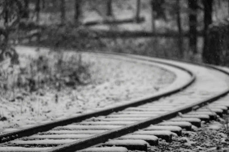 snow is falling on train tracks in the woods