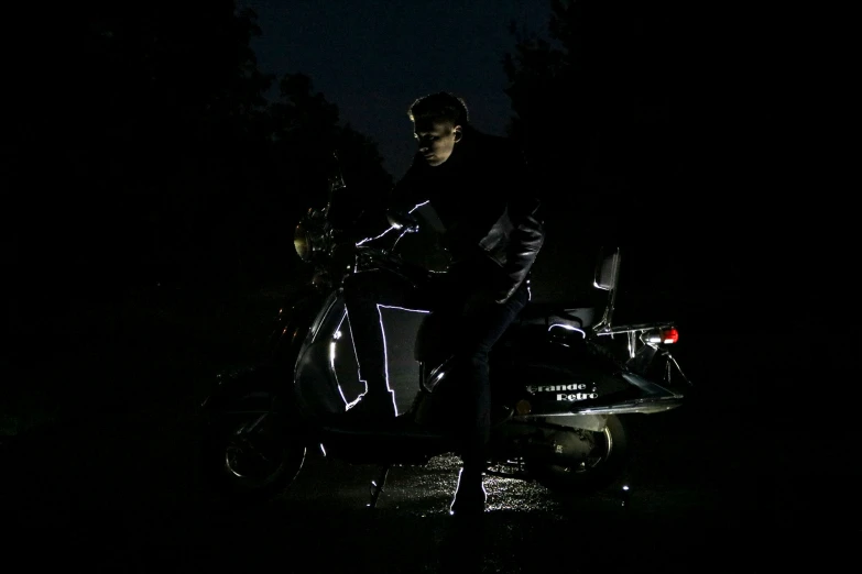 a man sitting on a motorcycle with his foot propped up against the motorcycle at night