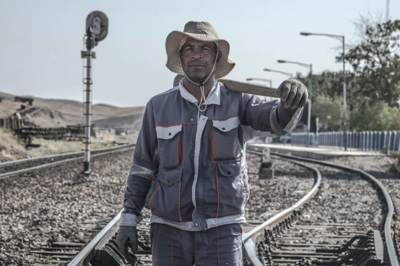 a man holding a giant piece of pipe as he stands on a train track