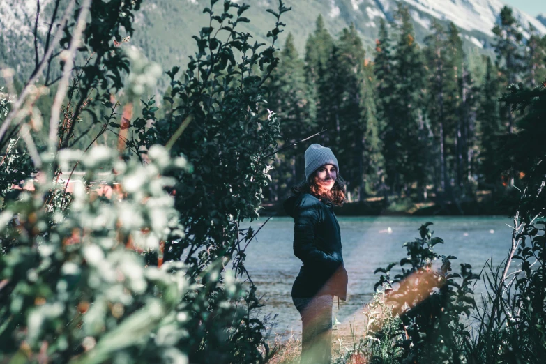 woman wearing winter clothes is standing near the edge of a lake