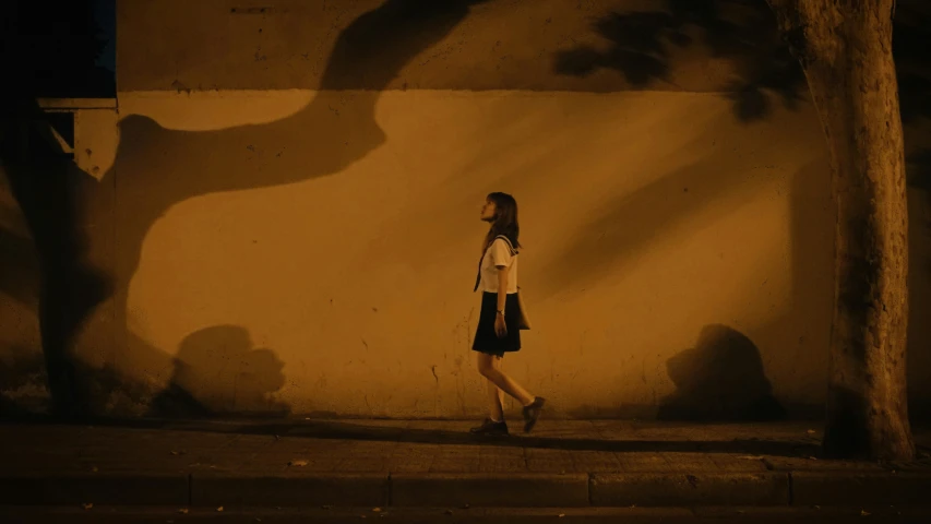 a woman walking down a street by the side of a wall