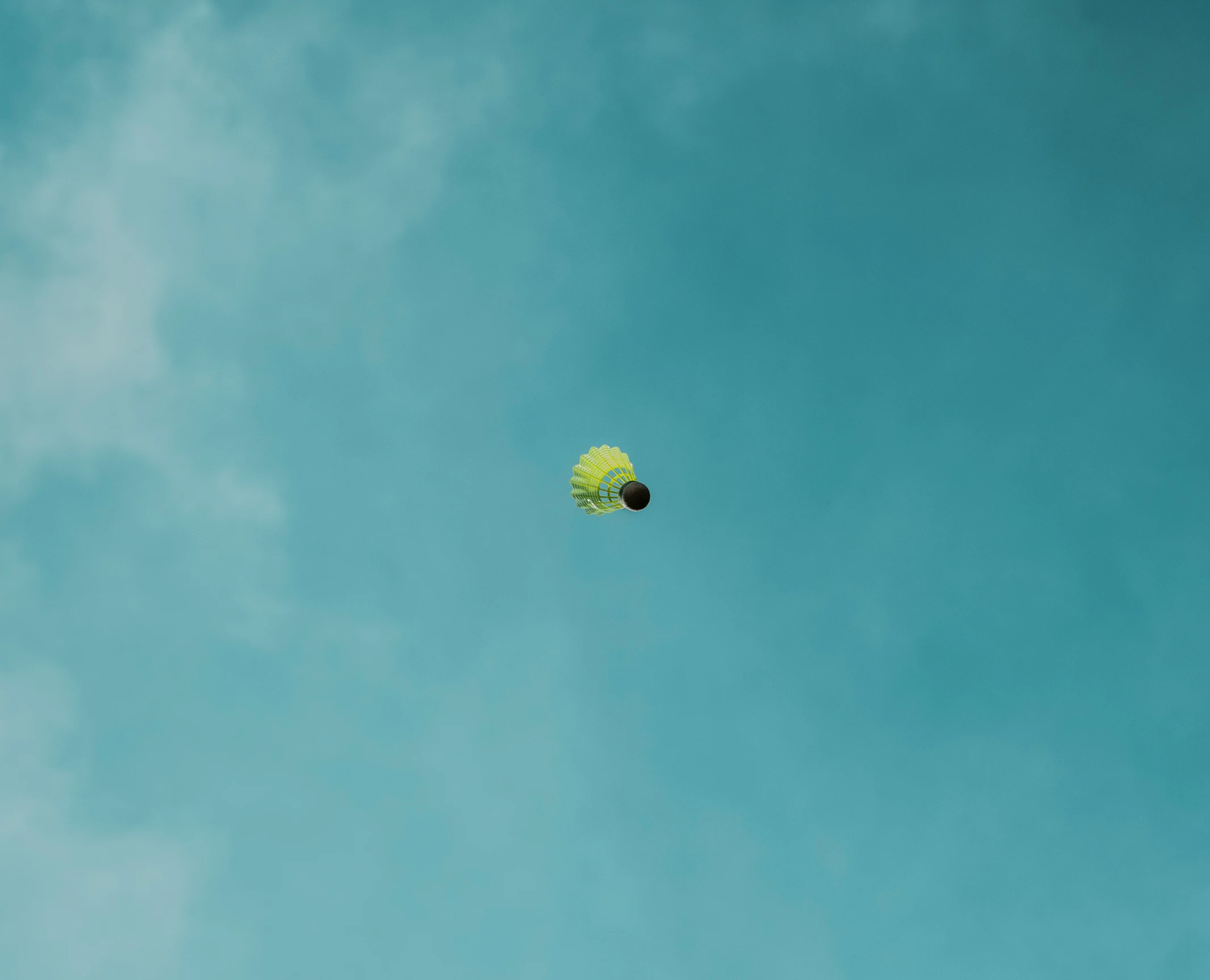 a green and yellow kite in the sky with a single cloud