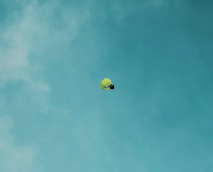 a green and yellow kite in the sky with a single cloud