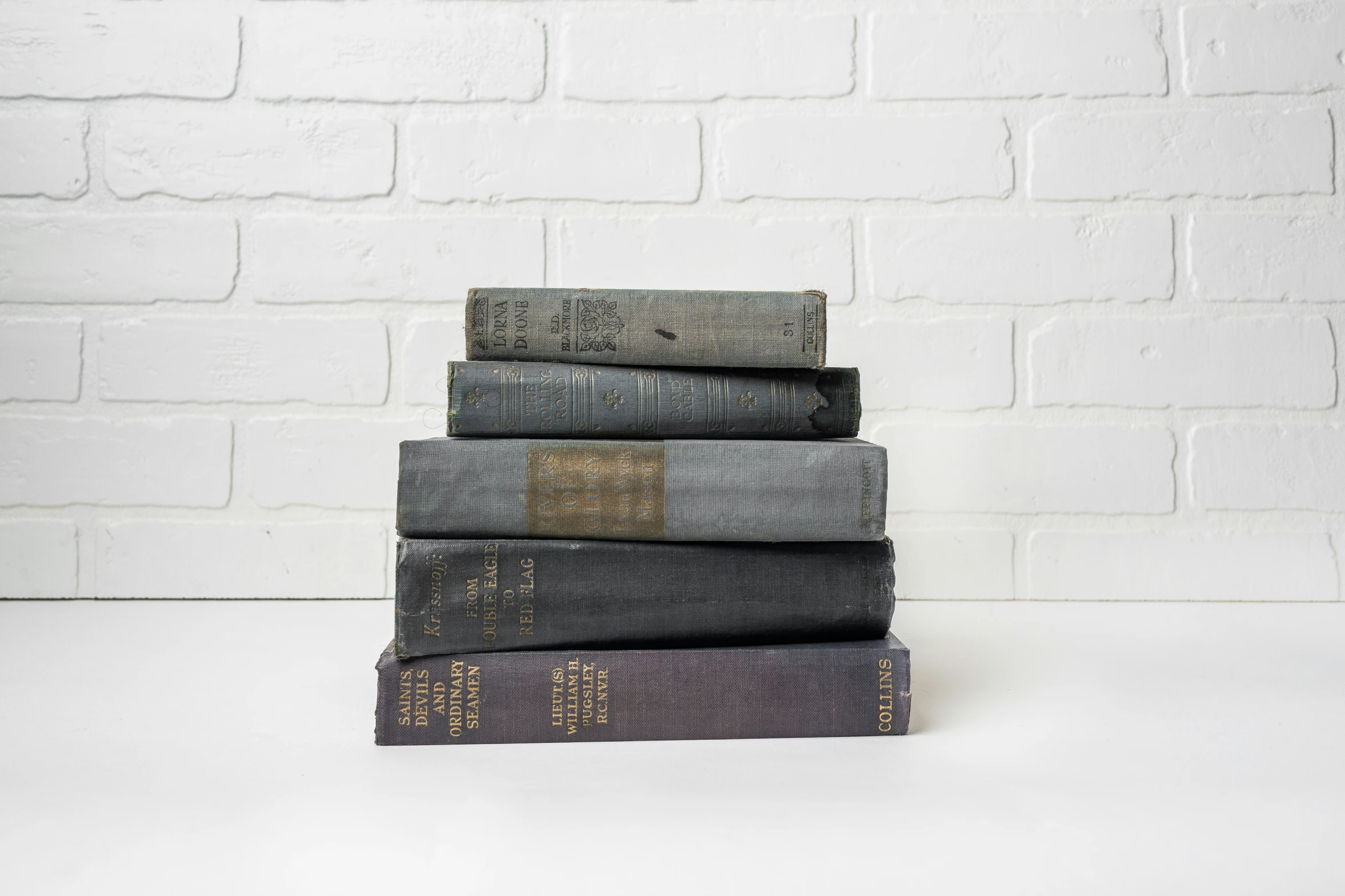 stack of four books sitting in front of a white brick wall