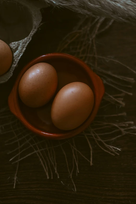 three eggs in a red bowl on the ground