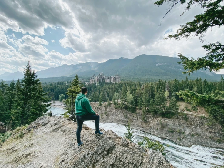 a man sitting on the edge of a cliff looking over a river