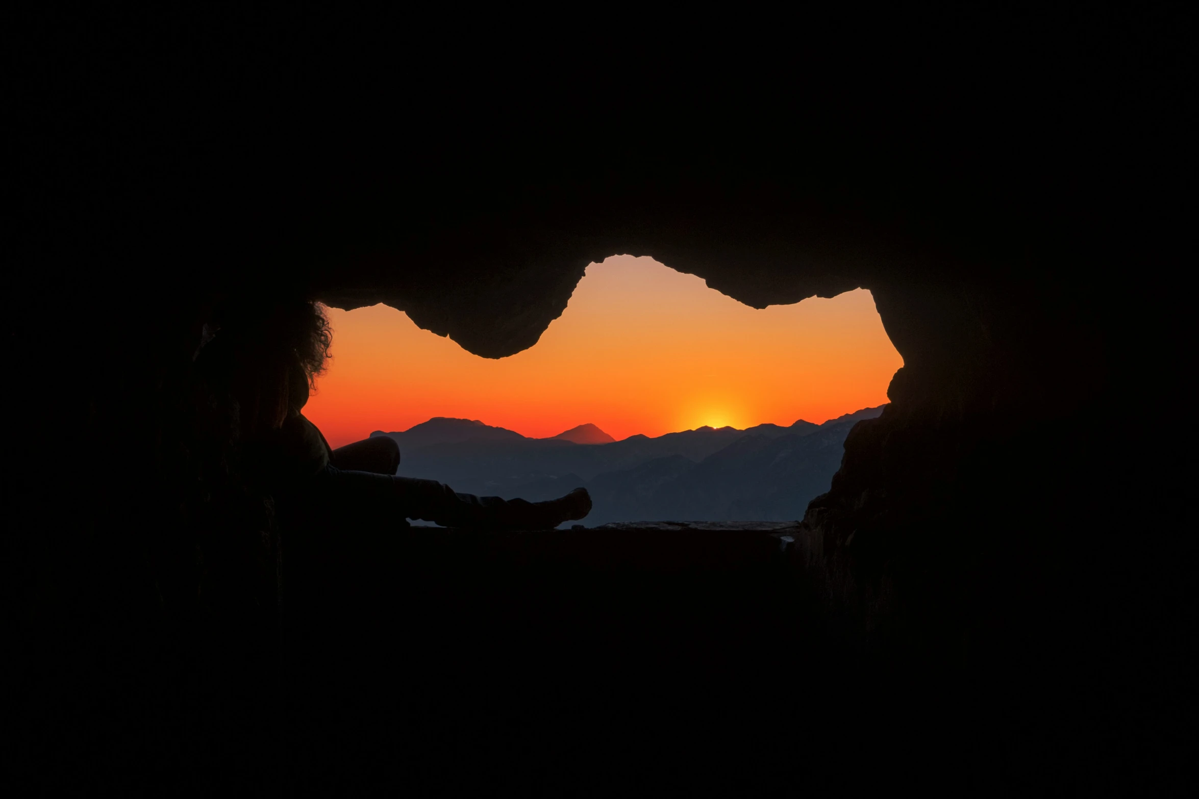 a man sitting in a cave during a colorful sunset