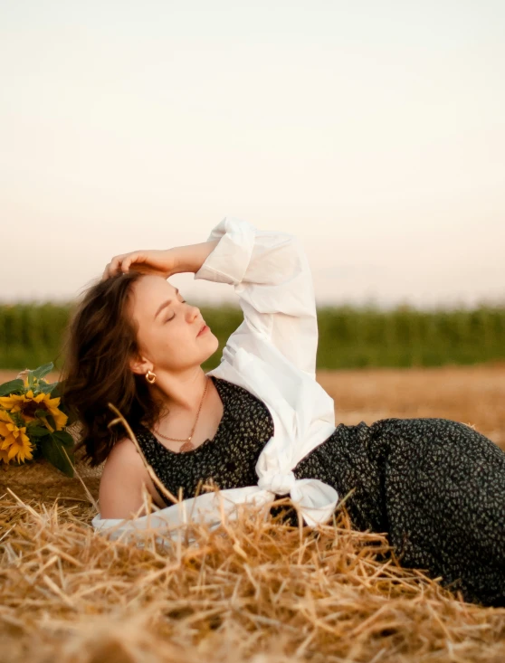 a woman laying down in some hay with a bunch of sunflowers
