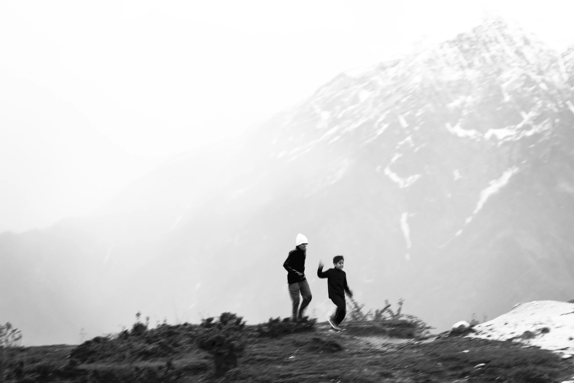 two hikers standing on a mountain overlooking snow - covered mountains