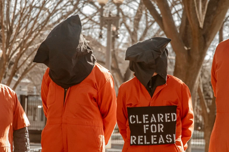 four people in orange suits holding a sign saying cleared for releasing