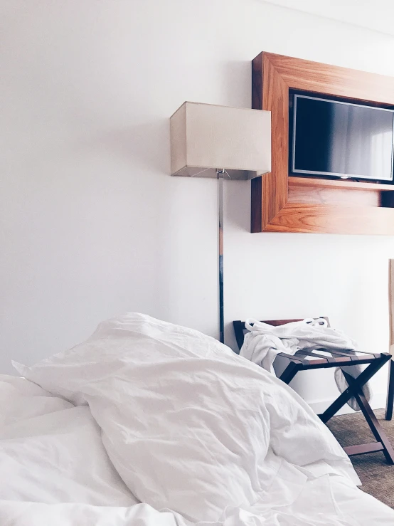 an unmade bed with white sheets, wooden headboard and flat screen tv mounted above