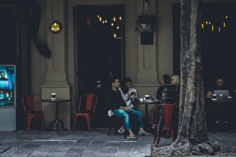 two people sitting outside on red chairs in front of a building