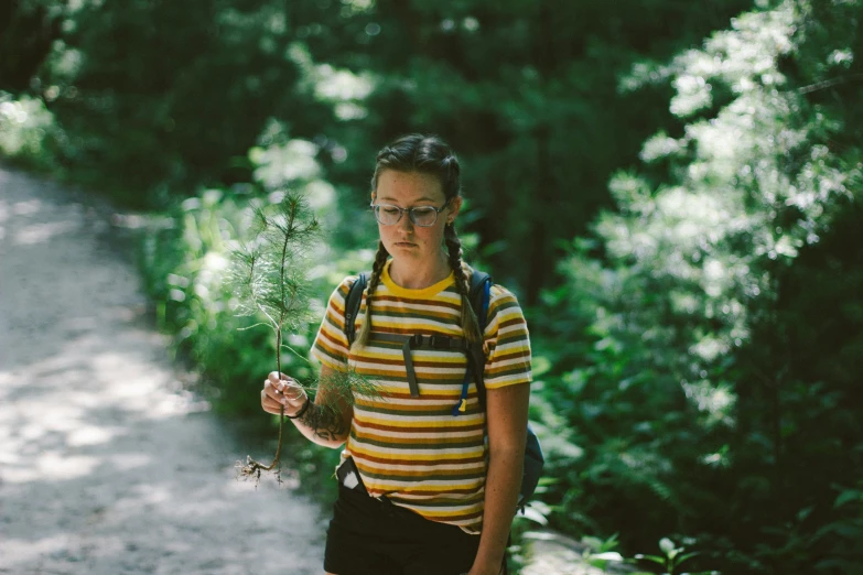 a girl in glasses and striped shirt holds out a flower in front of her