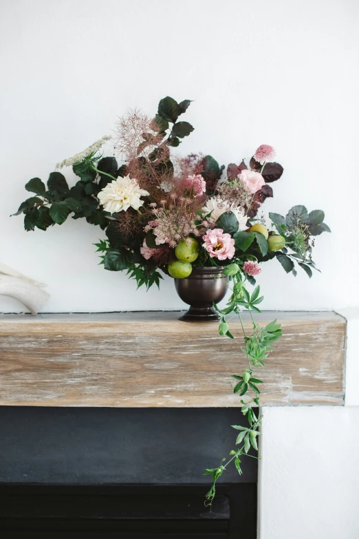 a vase with flowers, leaves and pears sitting on a mantle