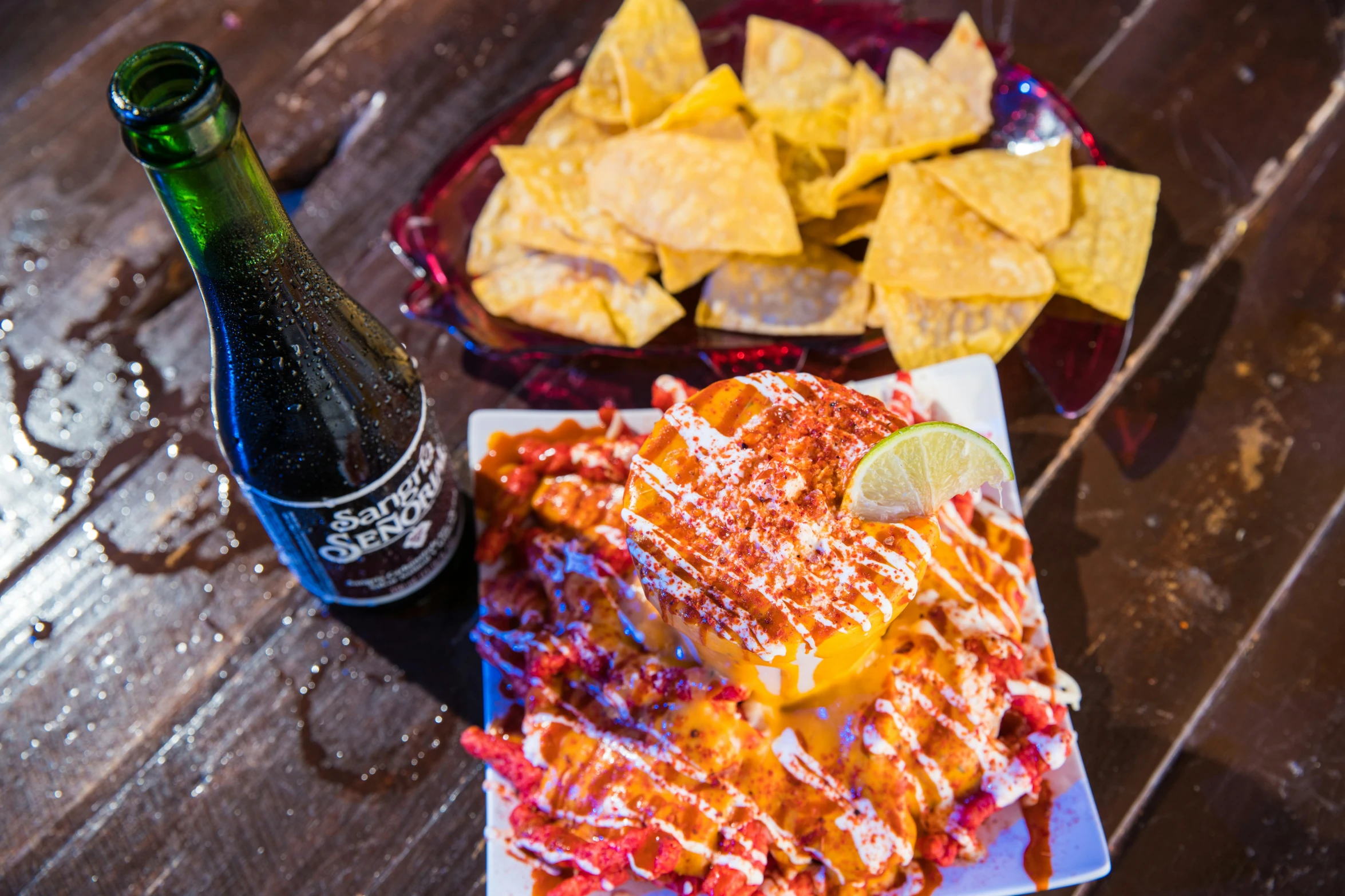 a meal on a plate next to a bottle of beer and a platter of nachos