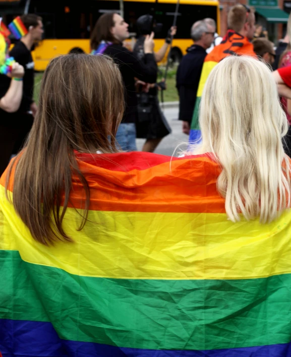 two girls wrapped in a rainbow colored blanket standing in the street