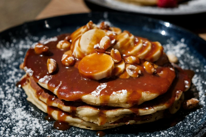 pancakes topped with banana slices and syrup on a black plate