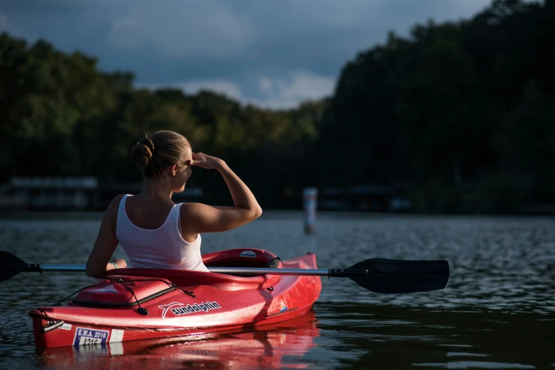 a woman paddling in a red boat on top of a lake