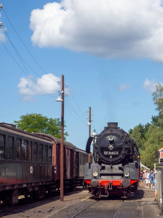 two trains at a train stop with many people near by