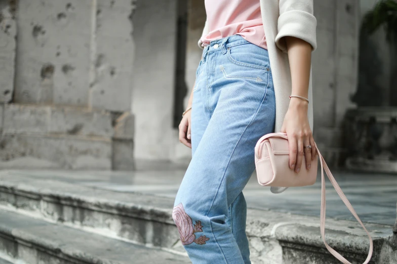 a woman wearing ripped jeans and a pink top holds a pink purse