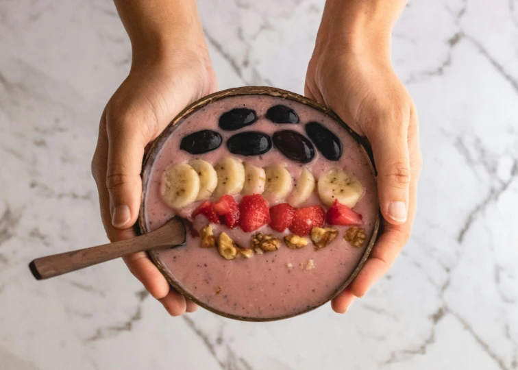 a woman holding a bowl of fruit with a spoon in it