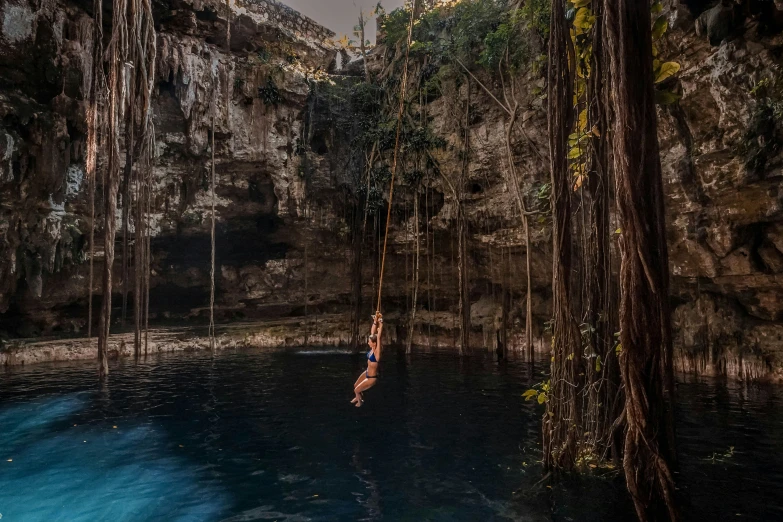 a woman in blue swimsuit jumping into a cave