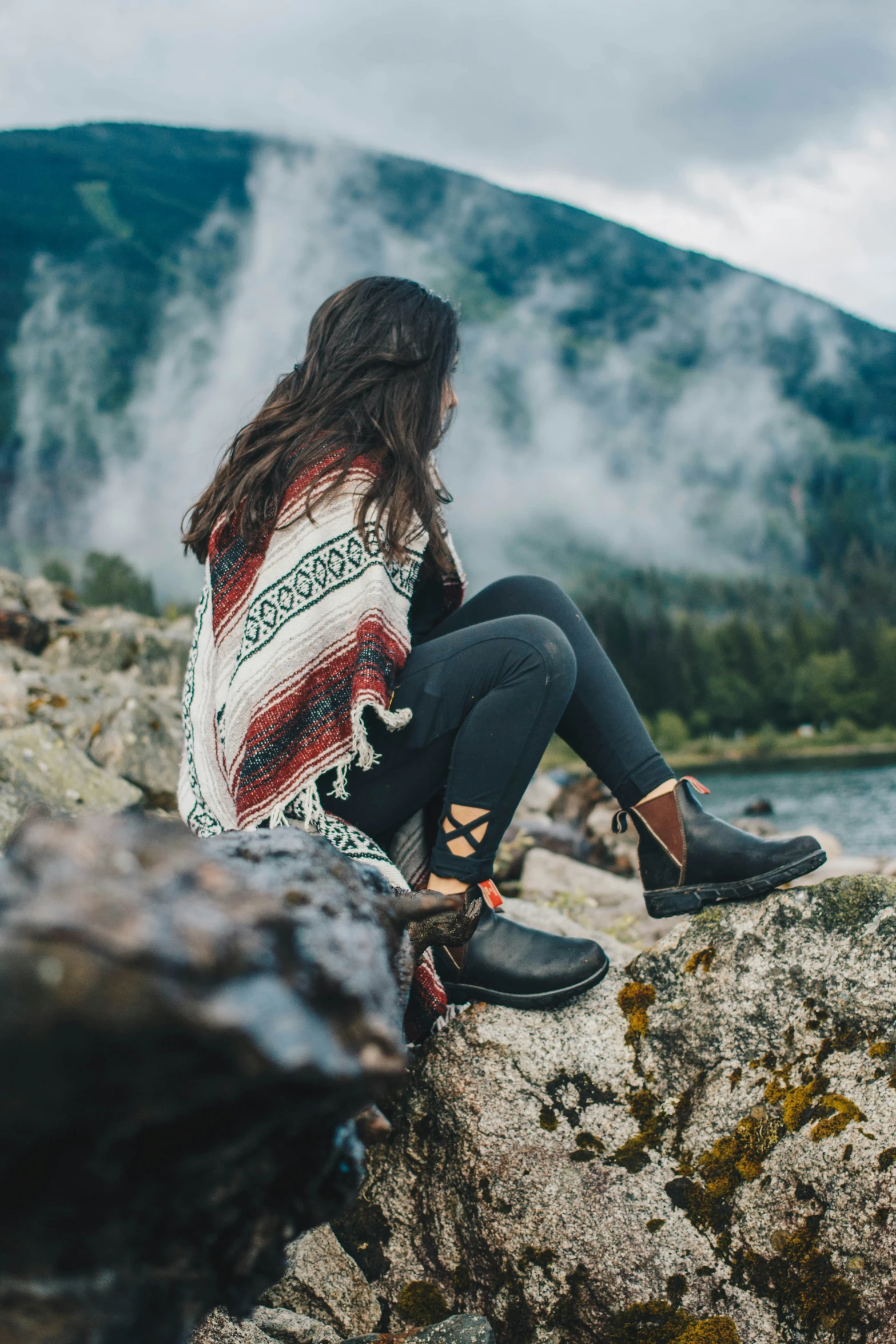 a woman sitting on rocks overlooking mountains and water