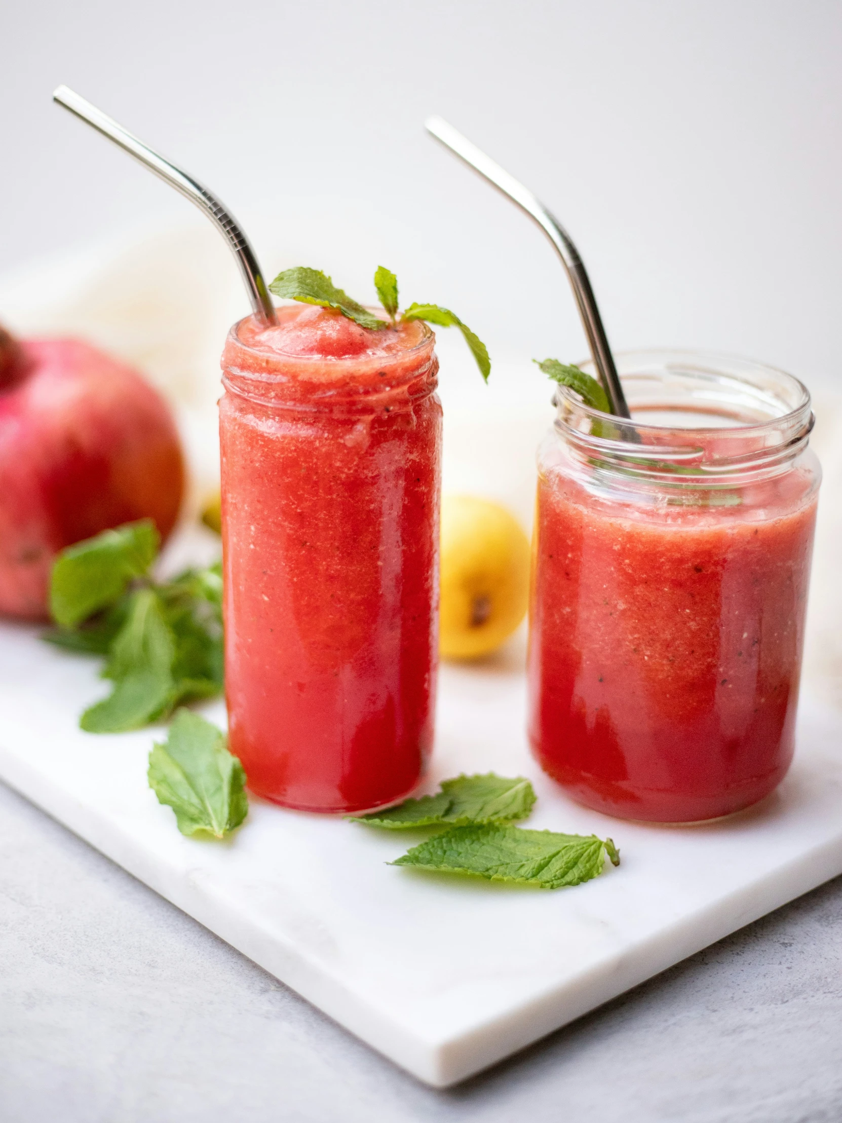 two jars filled with juice next to some strawberries