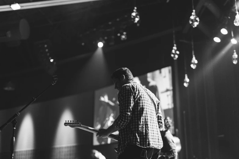 a black and white image of a man playing a guitar in a concert