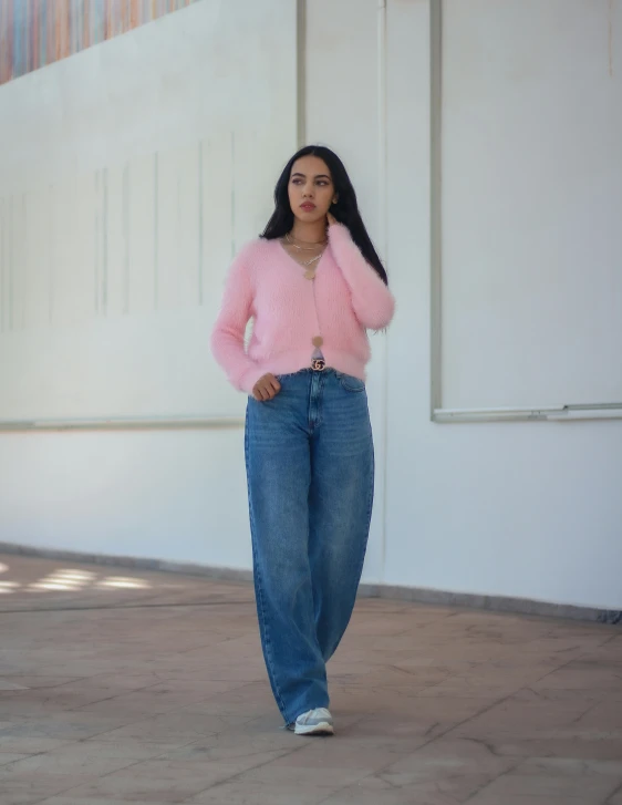  posing in denim pants and pink cardigan, in front of a building