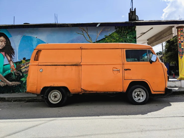 an orange van parked in front of a painting on a wall