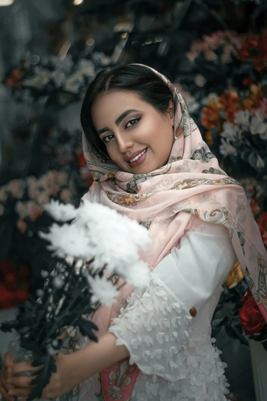 a woman smiles as she holds flowers and a large white vase