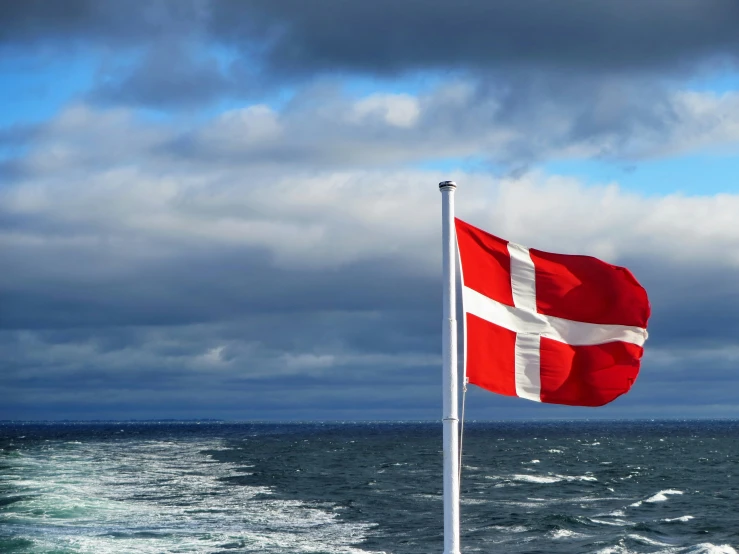 a red and white flag stands in the water next to a boat