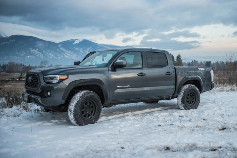 a silver truck is parked in the middle of a field covered in snow