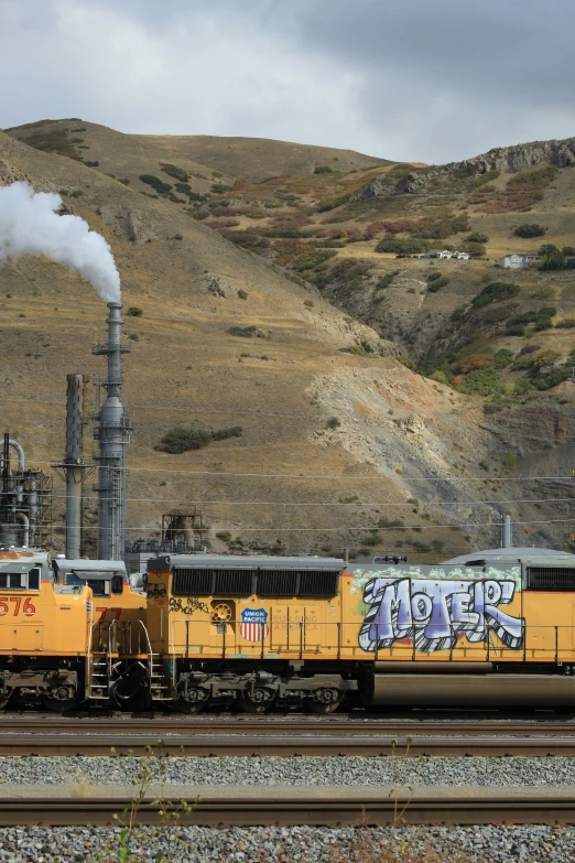 an orange train with black and yellow graffiti on it passing through a landscape