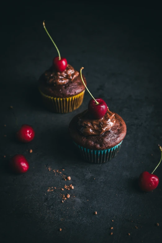 two chocolate cupcakes with cherry topping and one with red cherries